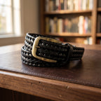 The Braided Leather Belt in Black, on a walnut executive desk [Black]
