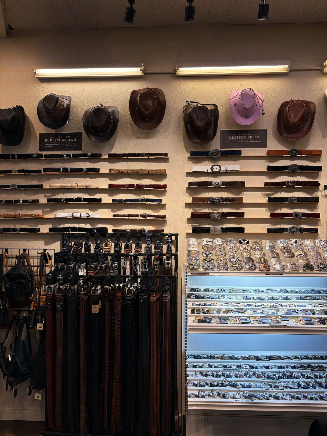 The belt wall: leather hats, the strap racks and the lit buckle case